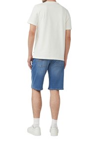 Weißes T-Shirt mit kurzen Ärmeln, blaue Denim-Shorts, weiße Sneakers und knöchellange Socken, von hinten betrachtet. Einfaches Design, lässiger Look.