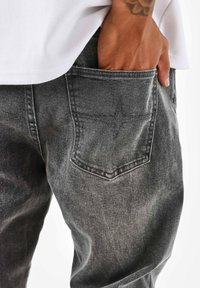 Vaqueros de mezclilla gris con un corte relajado, bolsillo trasero con detalles de costura y ligero desgaste. La tela presenta una apariencia suave y texturizada.