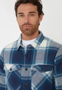 Blå og grå ternet flannel skjorte med knaplukning foran, to brystlommer og spids krave. Fremstillet af blødt tekstureret stof.