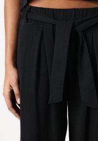 Black high-waisted trousers with a belt detail. Features pleats and a soft texture, made from lightweight fabric suitable for casual wear.