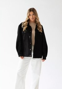 Czarna kurtka dżinsowa z długim rękawem, w oversize'owym kroju, z zapięciem na zatrzaski; posiada kieszenie na piersiach i kontrastowe mosiężne detale.