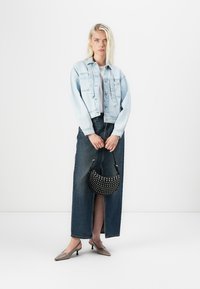 Light blue denim jacket over a white top, paired with a long dark denim skirt. Black handbag with studded accents and gray heeled shoes.