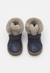 Mörkblå ankelstövlar med en mjuk beige pälsfåll, med tygremmar, gummisulor och en slät yta, designade för komfort och värme.