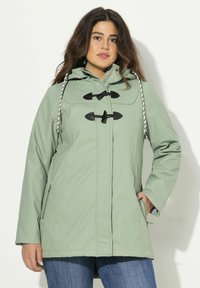 Ljusgrön vattentät jacka med huva, framknäppningar med snoddar och sidofickor. Har svarta detaljer och en strukturerad yta.