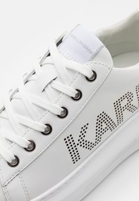 Białe skórzane sneakersy z perforowanym brandingiem "IKAR", płaskimi białymi sznurówkami, srebrnymi oczkami oraz wyściełanym językiem z metką z logo.