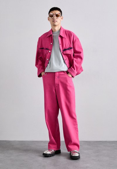 Ροζ τζάκετ από τζιν με θηλάκια, συνδυασμένο με ροζ παντελόνι με φαρδιά πόδια. Γκρι t-shirt από κάτω και ογκώδη μεταλλικά παπούτσια.