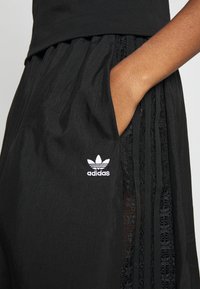 Svarta sportshorts med strukturerad yta, med spetsband vid sidorna och en broderad vit Adidas-logotyp framtill.