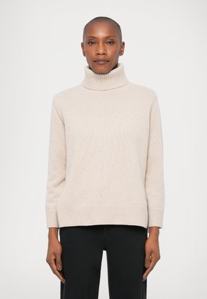 Pull en col roulé beige clair avec texture côtelée, manches longues et ourlet droit. Porté sur un pantalon noir, en matière tricot douce.