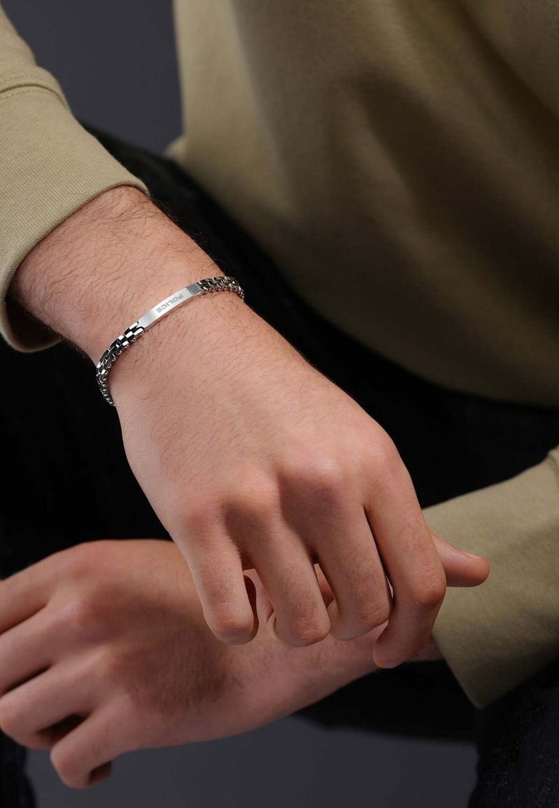 Bracciale in metallo argentato con catene nere, caratterizzato da una piastra di incisione rettangolare piatta sulla parte superiore. La texture è liscia e lucida.