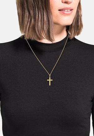 Collar de cadena fina con un colgante en forma de cruz dorada, llevado sobre un suéter negro de cuello alto. El colgante presenta un diseño simple y minimalista.