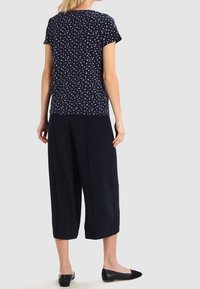 Top de manga corta azul marino con un estampado blanco, combinado con culottes amplios azul marino. La modelo lleva zapatillas negras. Diseño limpio y casual.
