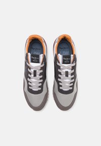 Graue und schwarze Sneakers mit Obermaterial aus gemischten Materialien, weißen Schnürsenkeln, orange-weißen Akzenten und einer strukturierten Gummisohle.