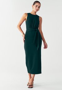 Robe maxi sans manches de couleur vert foncé, avec un corsage ajusté et un détail de taille nouée. Fabriquée en tissu lisse, elle présente une silhouette droite.