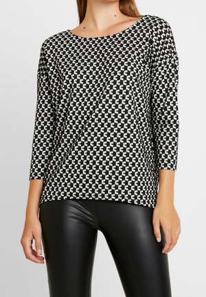 Langarmoberteil mit schwarz-weißer Musterung und Rundhalsausschnitt, das über ein geometrisches Design und eine lässige Passform verfügt, kombiniert mit schwarzen Leggings.