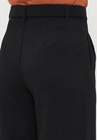 Black tailored trousers featuring a smooth texture, flat front with side pockets, and a fitted waistband.