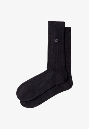 Par de calcetines cortos acanalados de color gris oscuro con un pequeño logo blanco de palos de golf cruzados y pelota cerca del puño superior.