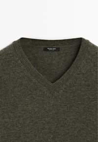 Maglione a V in verde scuro. Tessuto liscio e texturizzato con scollatura a coste e etichetta, che offre un design minimalista e una forma aderente.