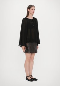Black sheer blouse with flowing sleeves, paired with a fitted brown leather skirt. Black flats with white polka dots. Simple vertical lines.