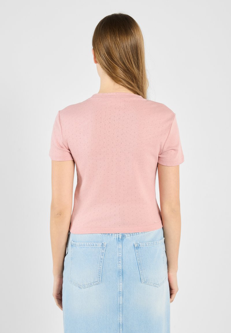Roze top met korte mouwen en een gestructureerd patroon, gepaard met een lichtblauwe denimrok. De pasvorm is ontspannen en eindigt op de taille.