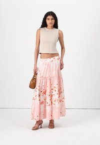 Béžový bezrukávový crop top s vysokým golierom; tiered ružová maxi sukňa s kvetinovým vzorom a volánikmi; hnedá kabelka; sandále na pásiky v nude farbe.