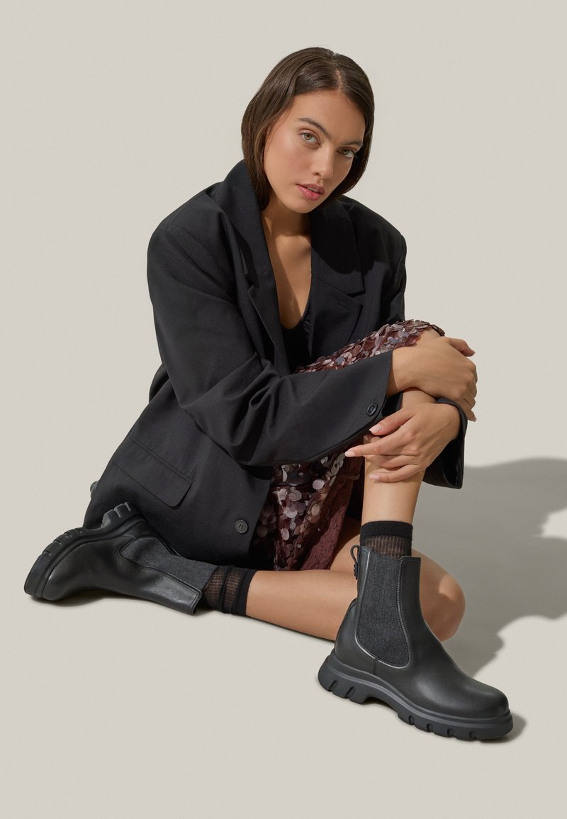 Bottines en cuir noir avec une semelle épaisse et des panneaux latéraux en élasthanne. Elles présentent des accents en tissu texturé et une finition lisse.