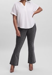 Weiße kurzärmelige, strukturierte Bluse, kombiniert mit schwarzen, hell auslaufenden Hosen mit einem metallischen glitzernden Muster und hellbraunen Absätzen.