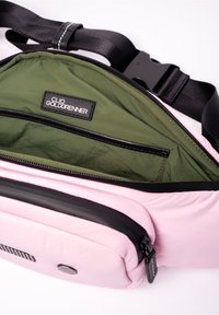 Roze schoudertas met zwarte rits en riem, geopend om de groene stoffen binnenkant en het merketiket "Clio Goldbrenner" te tonen.