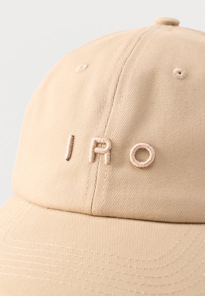 Casquette de baseball beige avec couture en relief formant le mot "IRO" sur le panneau avant, montrant la texture du tissu et les détails des coutures.