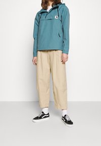 Lichtblauwe hoodie met een voorkeep, beige wijde broek en zwarte sneakers met witte zolen en veters.