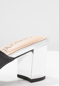 Svart slidesandalett med en glansig silverblockklack och en ljusbrun innersula med logodetalj. Släta ytor med en modern design.