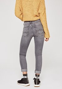 Jeans skinny grises con cintura alta y puños doblados. Presenta dos bolsillos traseros y una textura suave, combinados con un suéter amarillo texturizado.