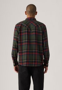 Long-sleeve plaid shirt featuring dark green, red, and yellow tones, with a straight hem and button cuffs. Classic check pattern and collar.