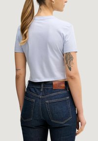 Jasnoniebieska krótka koszulka z krótkim rękawem. Ciemne dżinsy z denimu z brązową skórzaną metką na pasie i kontrastującymi przeszyciami. Gładka faktura.