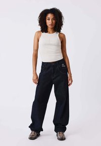 Light beige fitted tank top with embroidered detail, paired with dark blue wide-leg jeans featuring visible stitching and pockets. Casual shoes.