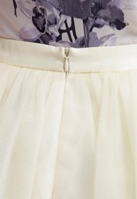 Ivory tulle skirt featuring a fitted waistband and a back zipper closure. The fabric is lightweight with a soft, sheer texture.