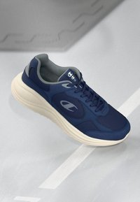 Navy blue athletic shoe with a mesh upper, padded collar, white sole, and contrasting logo detail on the side, featuring a rounded shape.