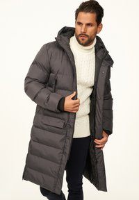 Langmantel in Anthrazitgrau mit Kapuze aus gestepptem Stoff. Ausgestattet mit einem Reißverschluss vorne, Druckknöpfen und zwei Seitentaschen.