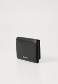 Portofel compact din piele neagră Calvin Klein, pliat, pe un fundal alb simplu.