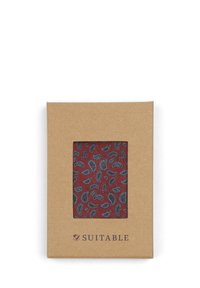 Rode stof met paisley-motief zichtbaar door een transparant venster van een bruine kartonnen doos, onderaan gelabeld met "SUITABLE".