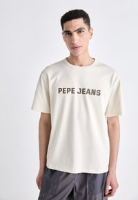 Korte ermer, kremfarget t-skjorte laget av bomull, med teksten "PEPE JEANS" i mørkebrune bokstaver på fronten.