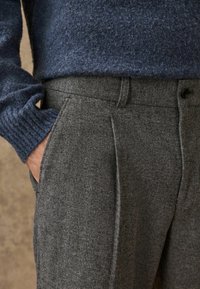 Gray tweed trousers with a subtle herringbone pattern, featuring side pockets and a smooth waistband. A dark blue knit sweater peeks from above.