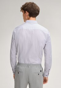Chemise à manches longues blanche avec motif géométrique bleu, complétée par un pantalon gris à taille élastique comportant deux poches arrière et des fermetures à bouton.