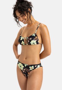 Zwarte bikini met bloemmotief; het bovenstuk heeft een centrale uitsnijding en verstelbare banden; de onderkant heeft een hoge snit met bijpassende prints.