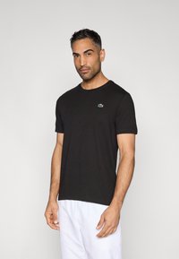 Czarna bawełniana koszulka z krótkim rękawem, okrągłym dekoltem i małym zielonym logo na lewej piersi.