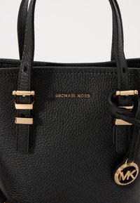 Sac à main en cuir noir avec texture granuleuse, matériel doré, détail du logo et deux poignées supérieures solides. Design compact et structuré.