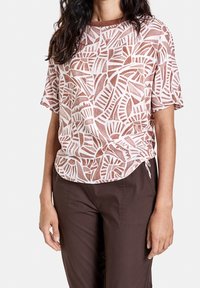 Kortærmet top lavet af lette materialer med et pink og hvidt bladmønster, der har en rund halsudskæring og diskrete side detaljer.