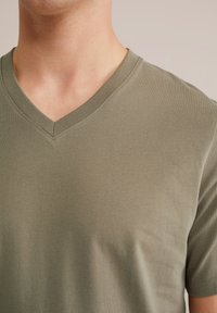 Olivno zelen T-shirt s V-izrezom, izdelan iz mehkega blaga, ki ima gladko teksturo, kratke rokave in našit izrez.