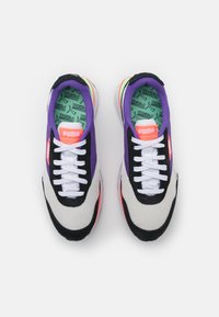 Paire de baskets Puma avec lacets blancs, panneaux noirs et violets, accents rose néon et semelles intérieures vertes avec logos Puma, vue d’en haut.