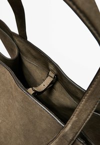 Olijfgroene suède tote bag met gladde leren bies, open bovenkant en interne sluitriem. Beschikt over een zachte textuur en eenvoudig ontwerp.