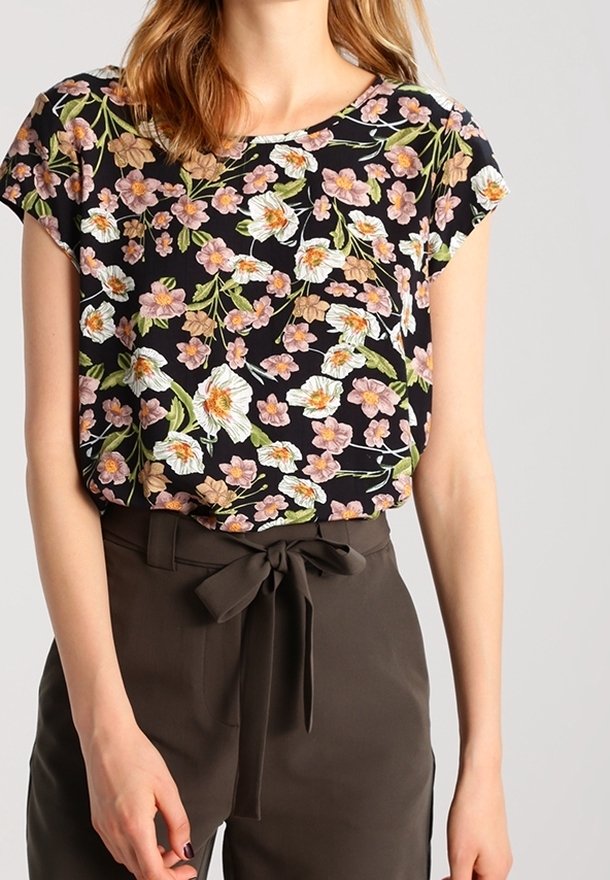 Blusa de flores de manga corta con fondo negro, con flores rosas y blancas. Combinada con pantalones oscuros de tiro alto color marrón con un lazo.